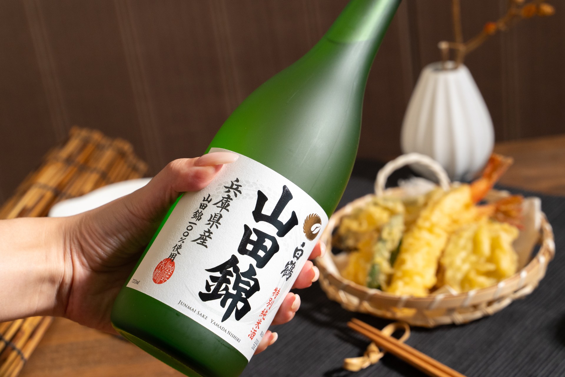 白鶴の山田錦の瓶を手に持ち、天ぷらとともに見せた日本酒の撮影写真