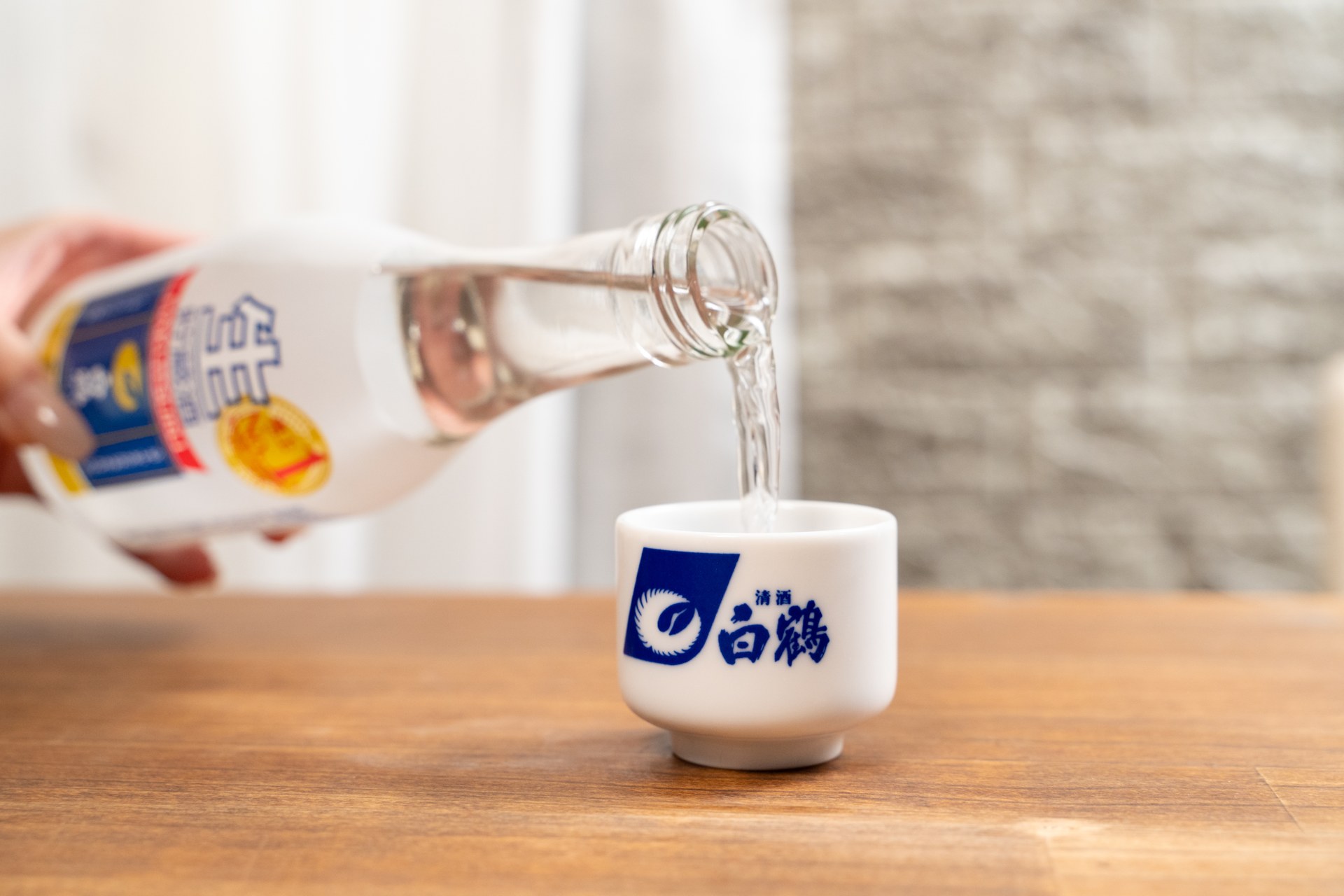 白鶴の日本酒をおちょこに注ぐ瞬間。液体の流れと瓶の質感を捉えた飲料撮影